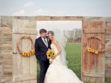 a cool outdoor barn wedding arch with a wooden gate and vine wreaths with sunflowers is a lovely and simple rustic wedding idea