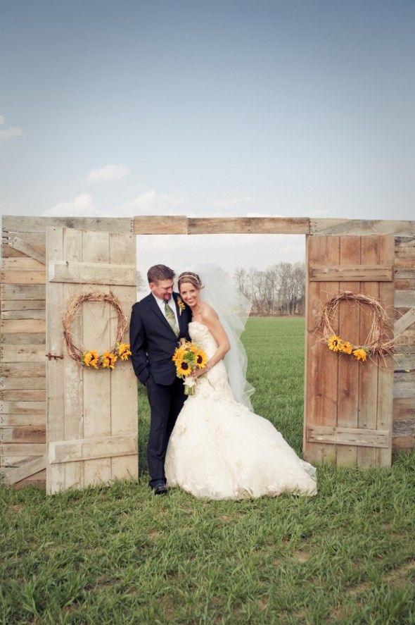 A cool outdoor barn wedding arch with a wooden gate and vine wreaths with sunflowers is a lovely and simple rustic wedding idea