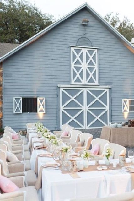 a refined and chic outdoor barn wedding reception space with comfortable chairs, white tableclothes and burlap runners plus neutral blooms