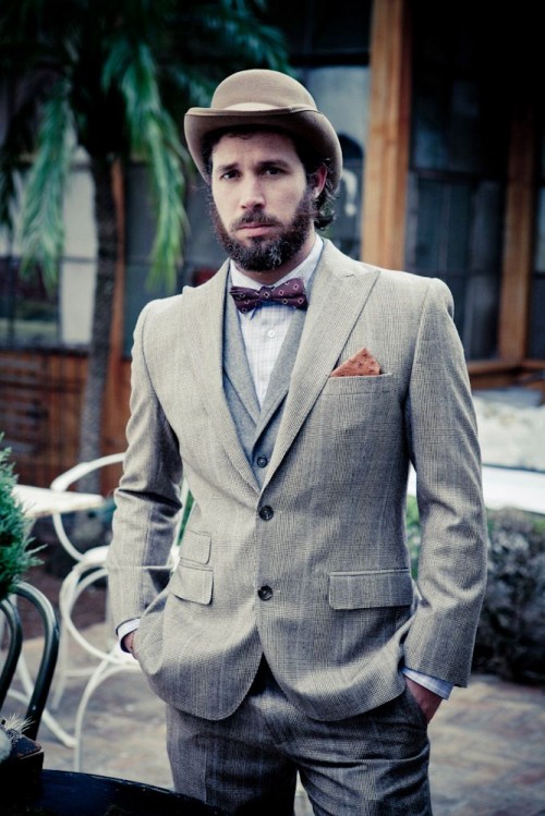 a vintage groom's look with a grey checked suit, a grey waistcoat, a burgundy printed bow tie and a hat