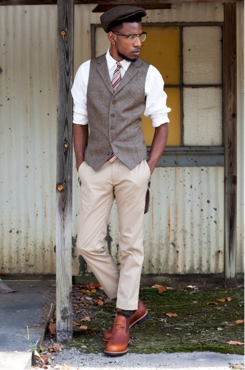 a stylish vintage groom's look with tan pants, a grey waistcoat, a white shirt, a striped tie, a brown cap and amber boots