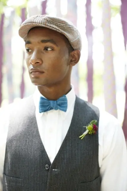a vintage groom's look with a white button down, a grey waistcoat, a blue bow tie and a cap