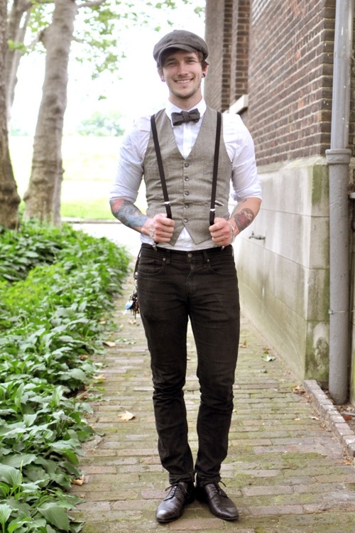 a vintage groom's outfit with black pants, a white shirt, a grey waistcoat, black suspenders and a brown cap