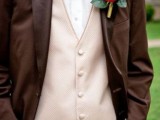 a brown suit, a neutral waistcoat and a matching bow tie plus a large floral boutonniere