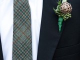 a black velvet suit, a white button down, a green plaid tie and a pinecone boutonniere