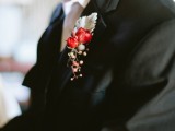 a black suit, a white button down, a black tie, a berry boutonniere plus pale greenery