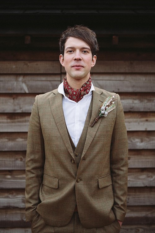 a brown three-piece wedding suit, a white button down, a red neck tie and a boutonniere