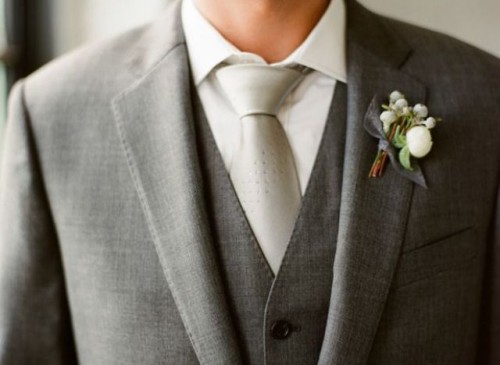a grey three-piece suit, a white button down, a shiny silver tie and a white floral boutonniere