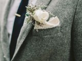 a grey tweed suit with a white button down, a navy tie and a white floral boutonniere