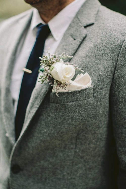 a grey tweed suit with a white button down, a navy tie and a white floral boutonniere