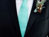a black suit, a white button down, a mint green tie and a winter boutonniere with pinecones and evergreens