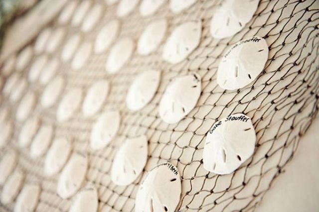 fishing net with white seashells and names written on them is a simple and fun way to display cards at the beach wedding