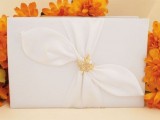 an elegant white wedding guest book accented with leaf drapery and a a gold leaf on top is refined