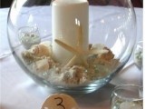 an aquarium with sand, seashells and starfish plus a pillar candle for a beach or seaside wedding