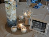 a jute rug, candles in candle holders, a vvase with blue crystals, white orchids and a vase with sand and starfish