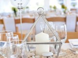 a metallic lantern with sand and pebbles and a large candle for a beach wedding