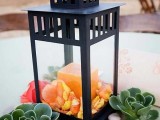 a black lantern with an orange candle, petals and succulents around for a summer or fall wedding