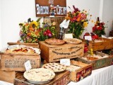 a stylish rustic fall wedding bar with homemade fruit pies served on crates and bright fall flowers for decor