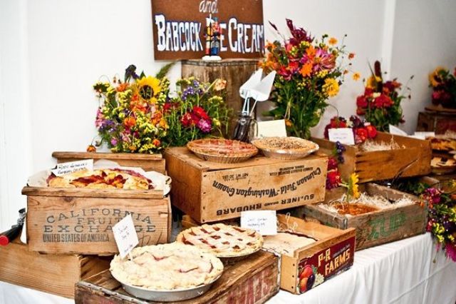 A stylish rustic fall wedding bar with homemade fruit pies served on crates and bright fall flowers for decor