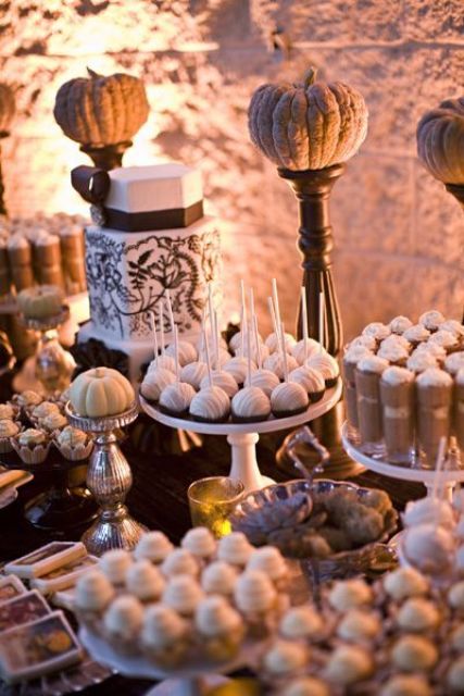 a white fall wedding dessert bar decorated with faux pumpkins on stands and candles
