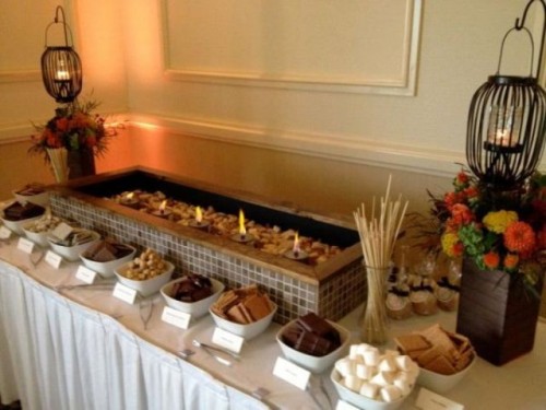 an s'more bar decorated with fall blooms and candle lanterns is a cool idea for fall and winter weddings