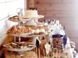 a rustic sweets bar with a stand with cookies on hay, a metal tray with candied apples, jars with macarons and a wedding cake