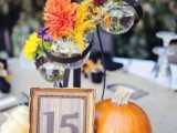 pumpkins, candles, a framed table number and bright flowers in creative sphere vases for a fall centerpiece