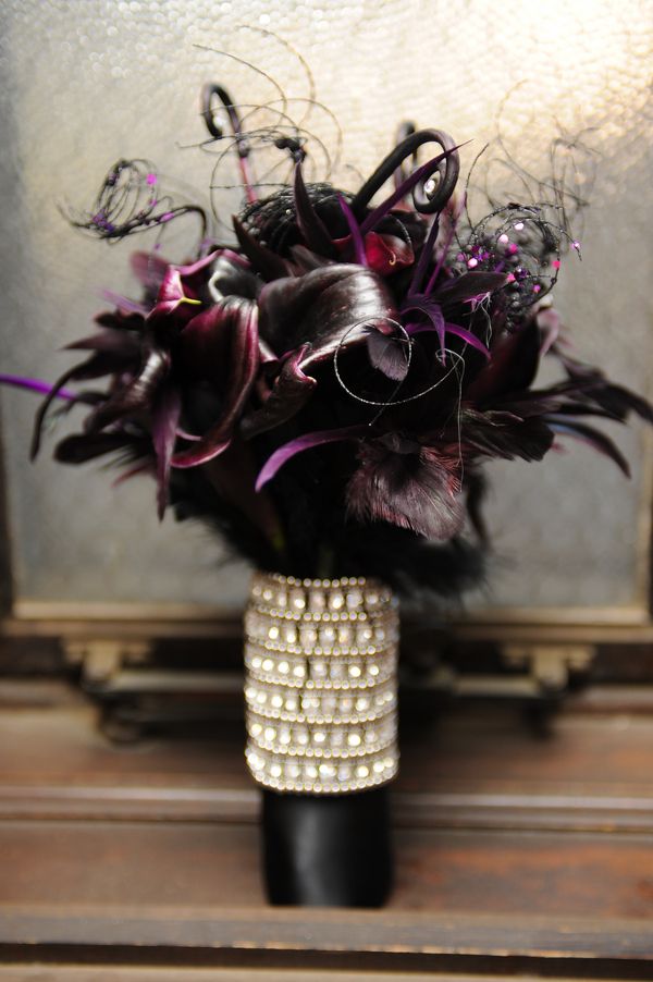 a sophisticated Halloween wedding bouquet of deep purple callas, feathers, lotus, twine with sequins and an embellished wrap