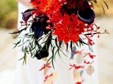 a bright Halloween wedding bouquet of red, orange and deep purple blooms, greenery and cascading red blooms
