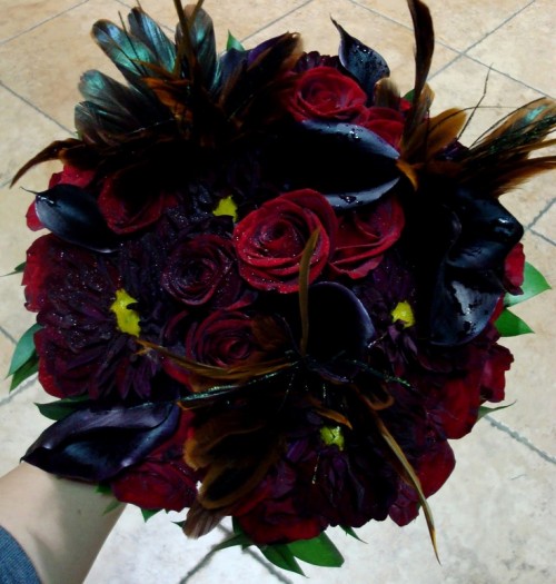 a dark Halloween wedding bouquet of red, burgundy and black blooms, with feathers and shiny touches