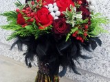 a bold Halloween wedding bouquet of red and burgundy blooms, lots of berries, greenery and black feathers