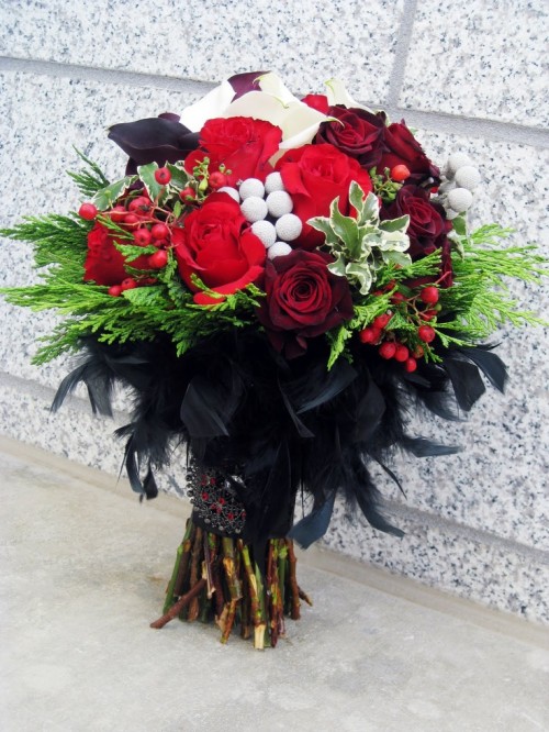 a bold Halloween wedding bouquet of red and burgundy blooms, lots of berries, greenery and black feathers