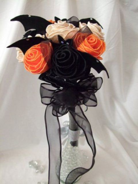 a fabric Halloween wedding bouquet of orange, black and white blooms and fabric bats plus a tulle bow