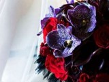 a dark Halloween wedding bouquet of red, purple, deep purple blooms and black feathers is very bold and stylish