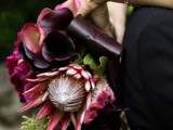 a refined dark Halloween wedding bouquet of pink and deep purple blooms, greenery and much texture is very chic