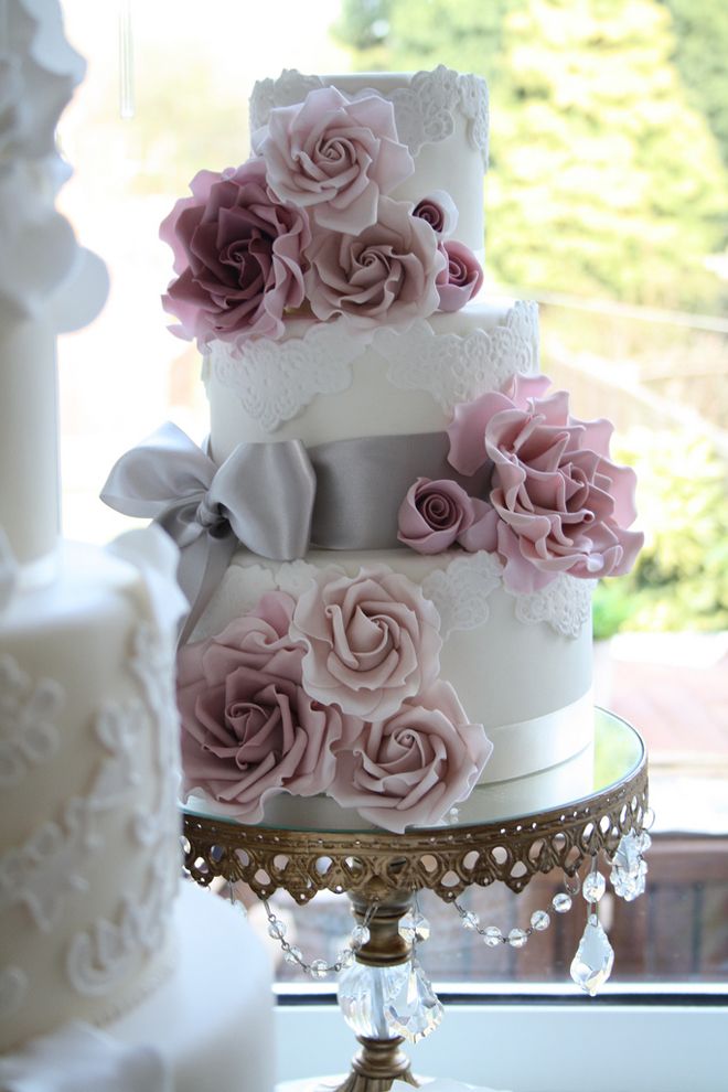 A romantic lace wedding cake with mauve and blush blooms and grey ribbons and a bow