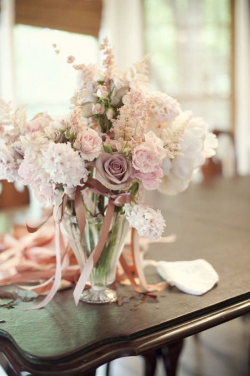 a tender wedding centerpiece with white, blush and mauve blooms and some ribbons
