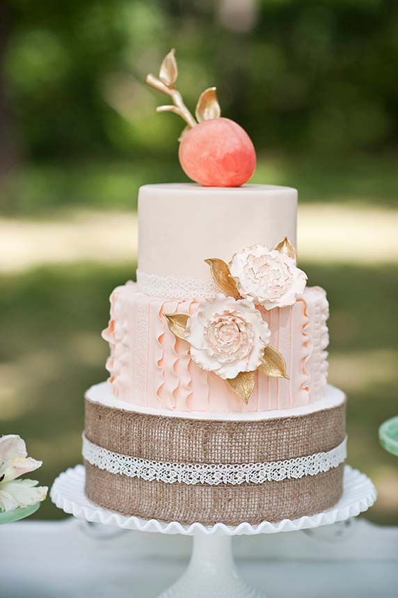 a beautiful wedding cake with a burlap tier, a peachy one, a neutral tier and a sugar peach with gold leaves on top