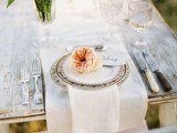 a chic wedding tablescape with neutral linens, printed plates, peachy blooms and greenery and refined cutlery