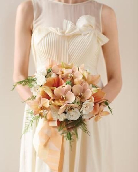 a delicate peach and cream wedding bouquet with peachy and rust blooms plus greenery and peachy ribbons is very elegant