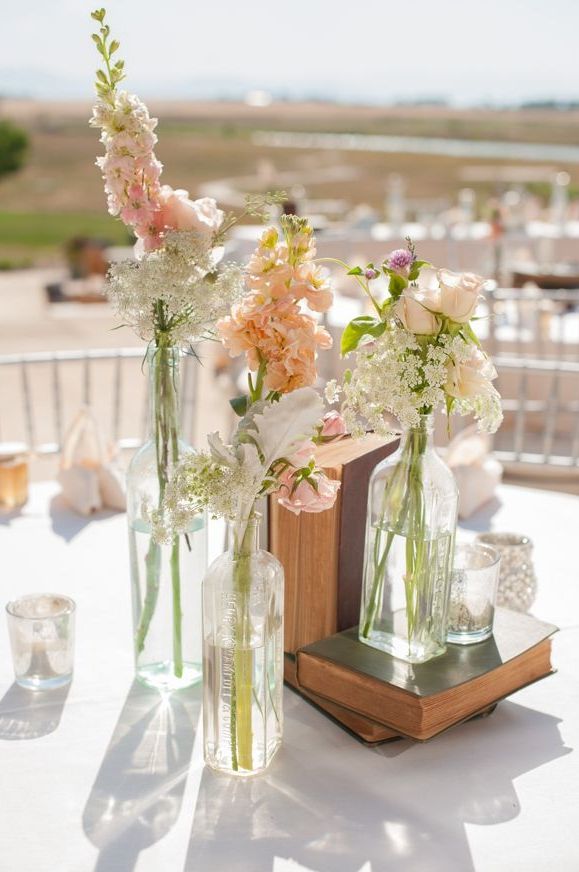 a vintage cream and peach wedding centerpiece of vintage books, peachy and pink blooms and white wildflowers is cool and chic