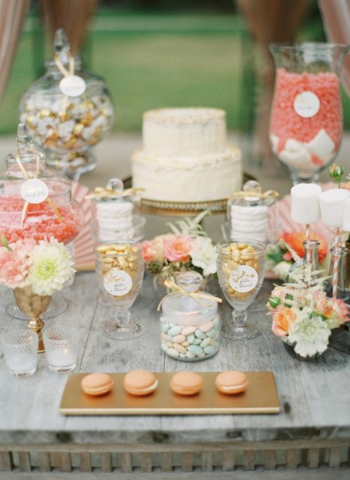 a lovely peach and cream sweets table with coral candies in jars, peachy macarons, peachy and coral blooms and greenery and leaves