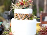 a white wedding cake decorated with ethnic print ribbons and bright succulents and air plants on top