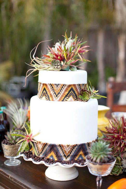 A white wedding cake decorated with ethnic print ribbons and bright succulents and air plants on top