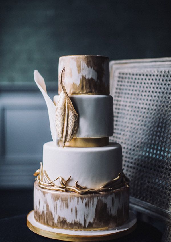 A whimsical gold and white wedding cake with an ikat tier, large gold leaves for decor