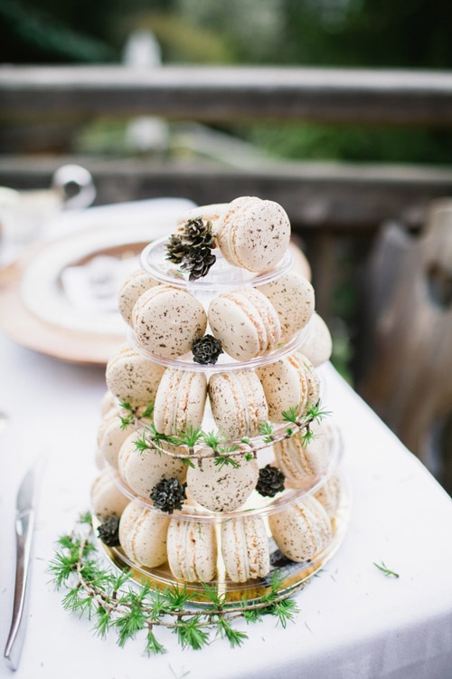 a clear stand with creamy macarons and greenery and pinecones is a lovely idea for a modern wedding, it's a cool solution to display them at your wedding