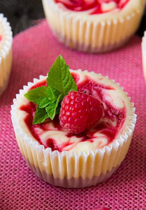 mini raspberry swirl cheesecakes with fresh berries and leaves on top are super tasty