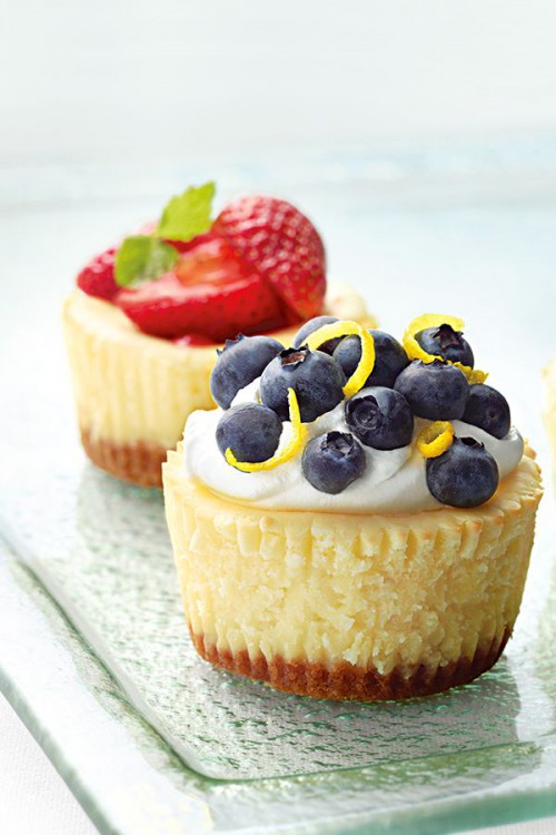 mini cheesecakes with strawberries and blueberries on top, with cream and fresh zest