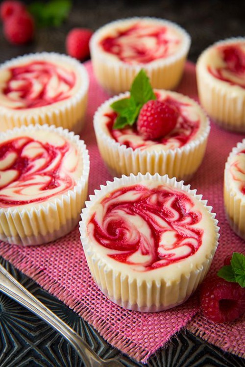 raspberry swirl mini cheesecakes with fresh berries on top and some leaves