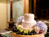 a cheese wheel tower topped with blooms and fresh grapes is a gorgeous idea for a vineyard wedding, if you don’t want any sweets